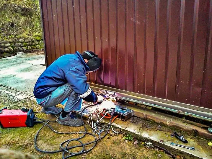 Muž opravuje posuvnou bránu svépomocí svařováním u základu.
