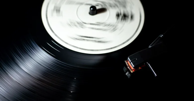 Gramofon s jehlou a otáčejícím se vinylem na černém pozadí.