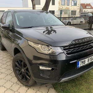 Černé střední SUV Land Rover Discovery zaparkované na dlažbě.