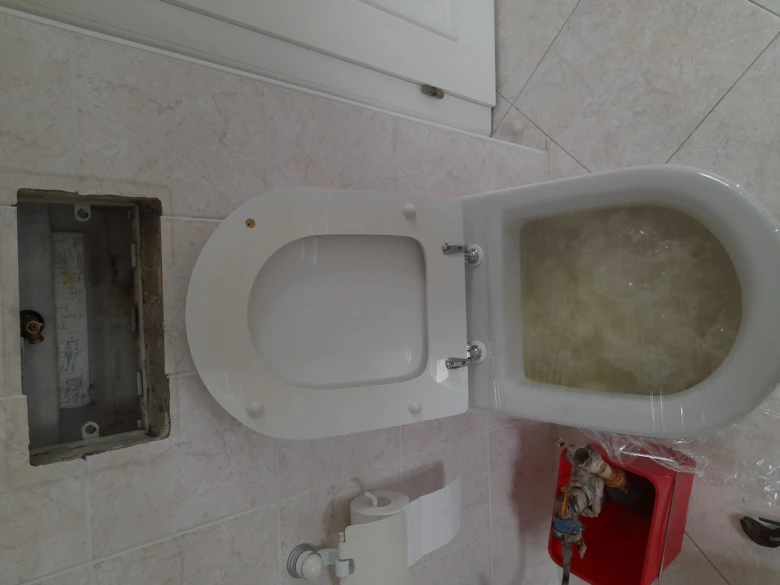 Záchodová mísa s otevřenou víkem a viditelným vodním zásobníkem.